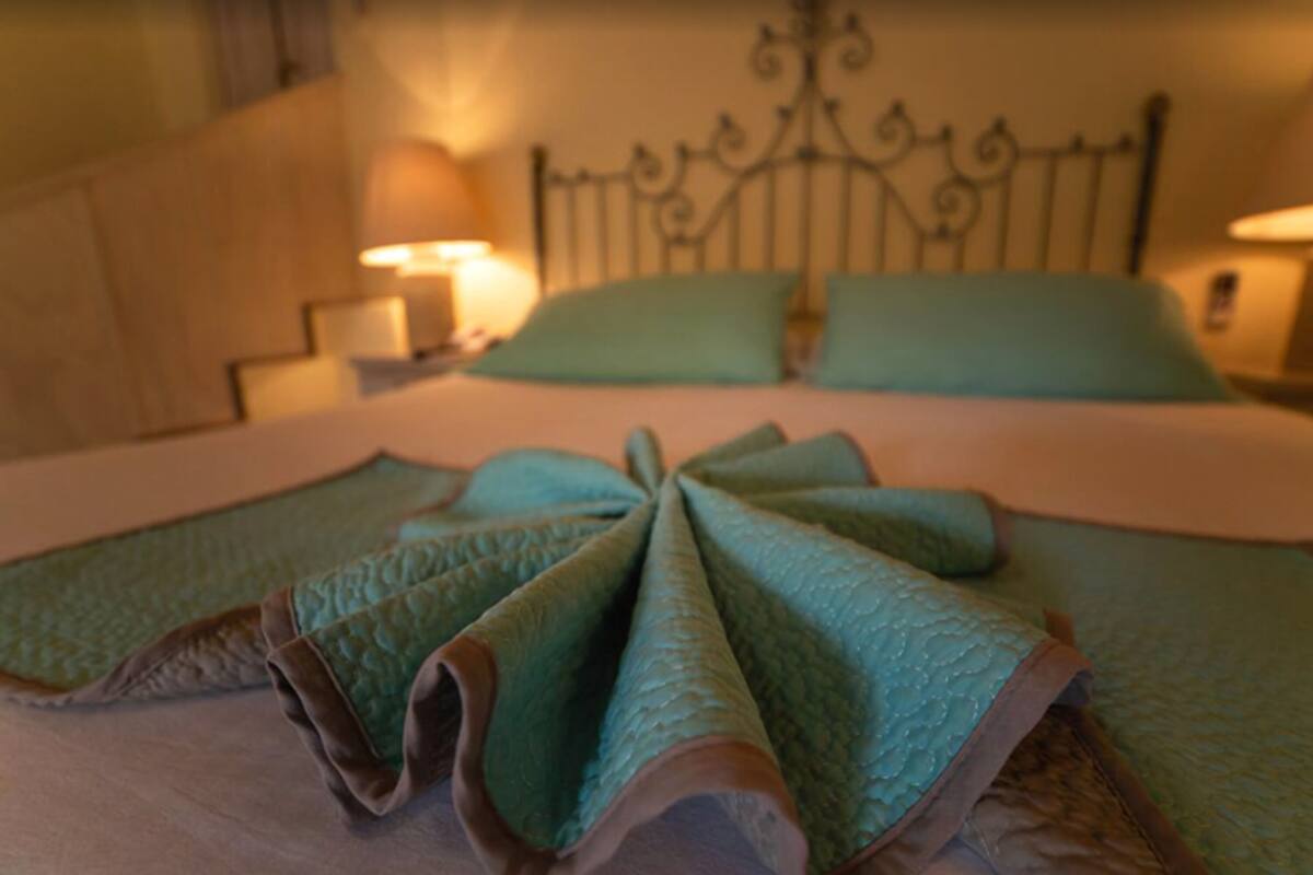 A neatly made bed with a green blanket and pillows, a metal headboard, and bedside lamps.
