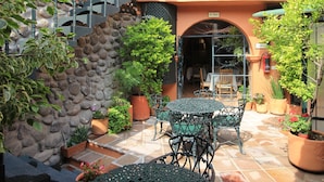 A courtyard with a stone wall, potted plants, a metal table with chairs, and a staircase leading to an upper level. - Villa Mirasol Hotel (San Miguel de Allende)