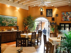 A dining area with wooden tables and chairs, a ceiling fan, and a large painting on the wall. - Villa Mirasol Hotel (San Miguel de Allende)