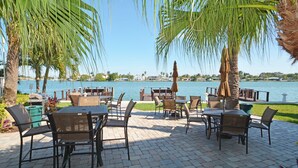 Un patio al aire libre con mesas y sillas, palmeras y vista al agua.