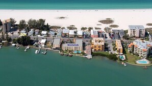 Vista aérea de una zona hotelera costera con varios edificios, una playa y barcos.