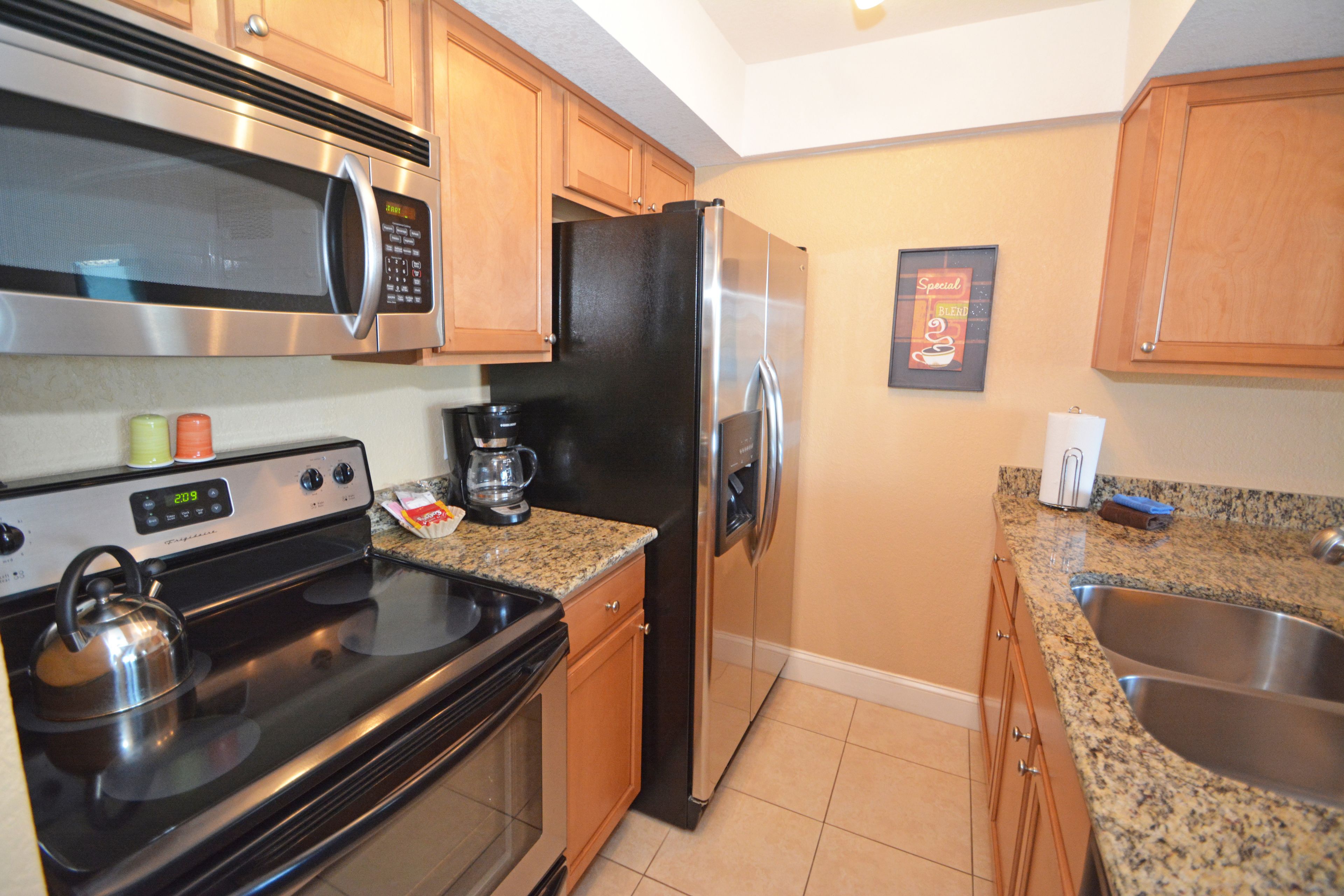 A kitchen with a stainless steel microwave, stove, refrigerator, and granite countertop.