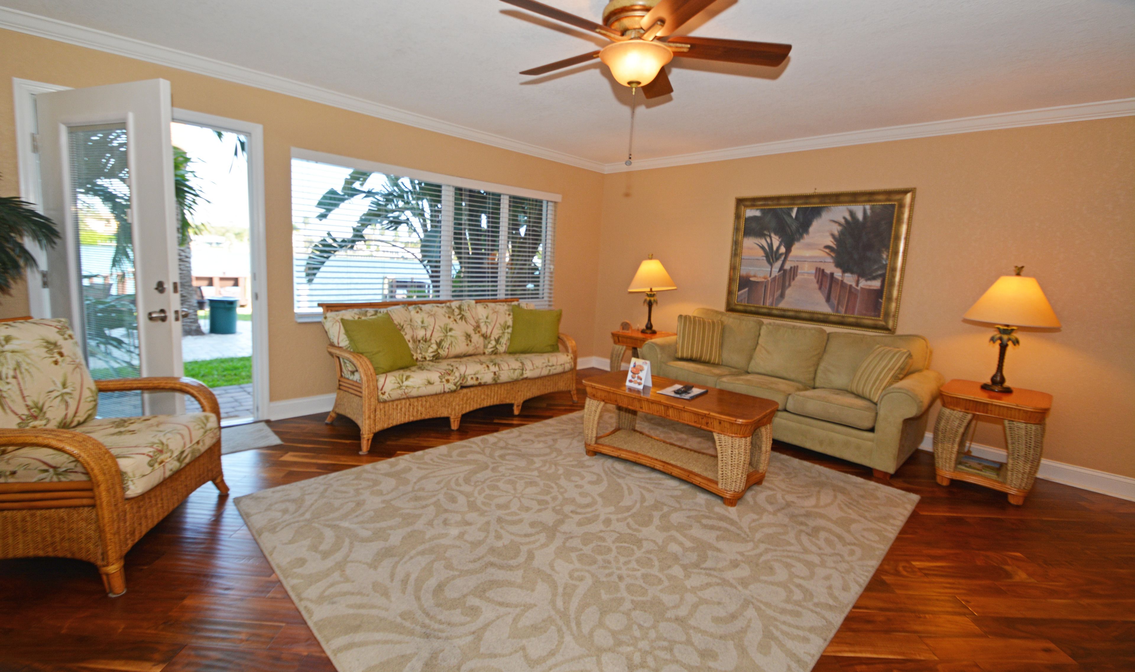 A living room with wicker furniture, a ceiling fan, and a large window with blinds.