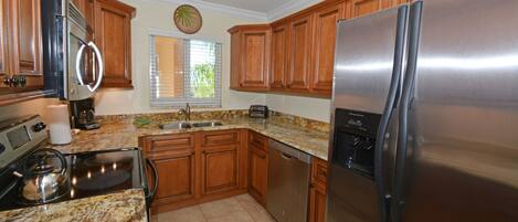 A kitchen with wooden cabinets, a stainless steel refrigerator, a built-in oven, and a granite countertop.
