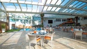 A spacious indoor area with a glass ceiling, a pool, and outdoor seating. - Bristol Hotel (Amman)