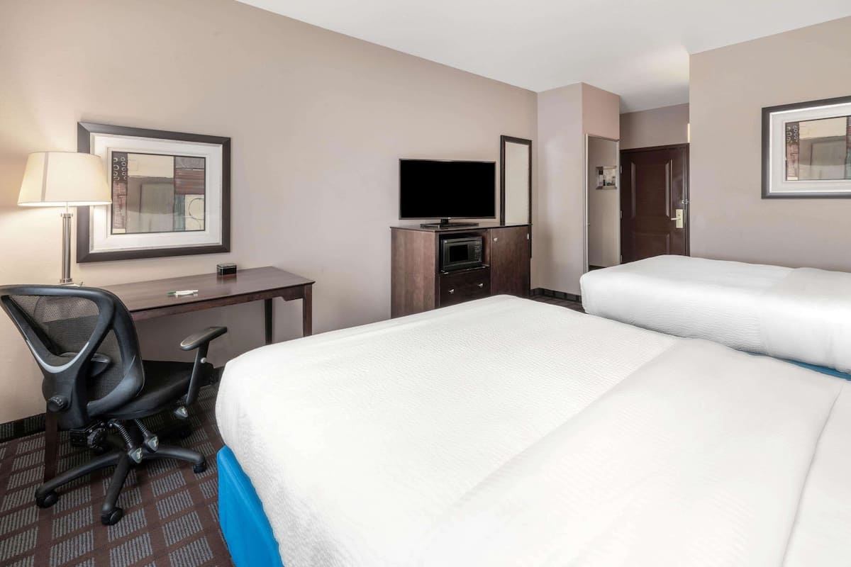 A hotel room with a bed, a desk with a chair, a TV, and a microwave.