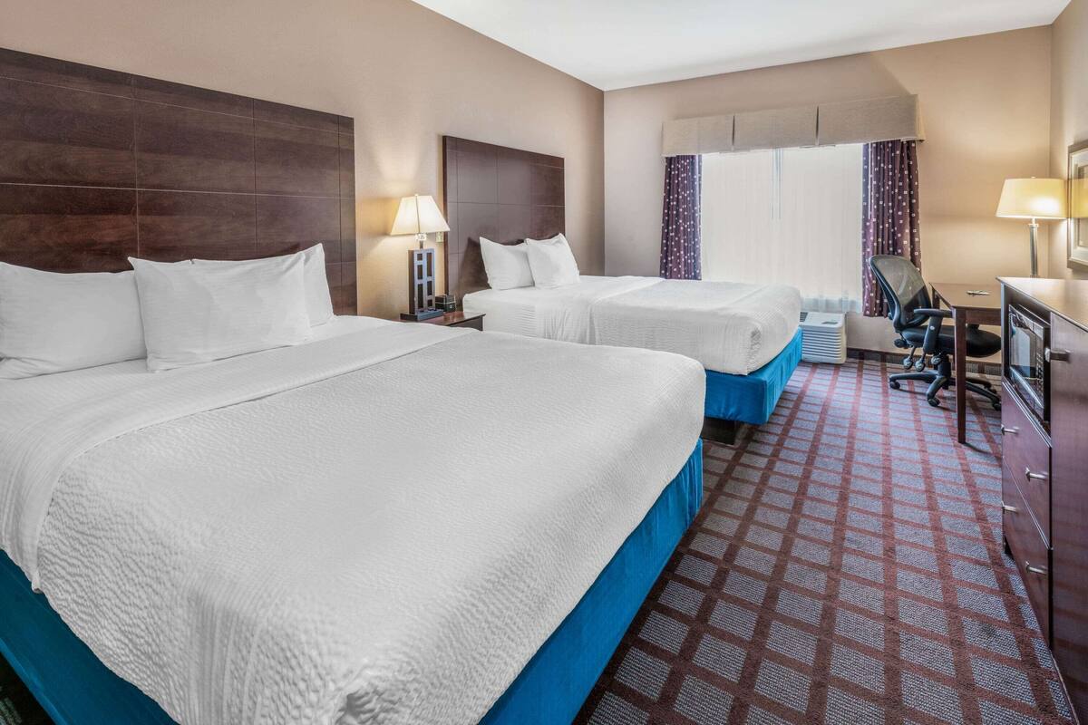 A hotel room with two beds, a desk, a chair, and a window with curtains.