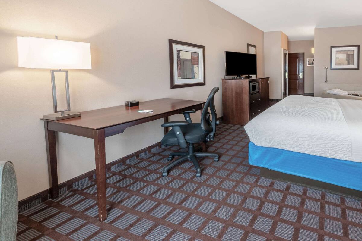 A hotel room with a bed, desk, chair, TV, and a bathroom.