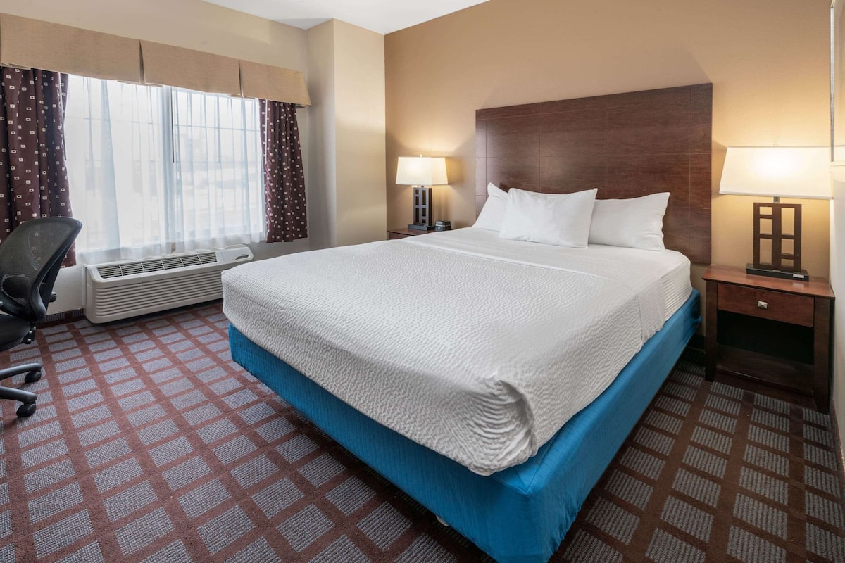 A hotel room with a large bed, two bedside tables with lamps, a desk, and an air conditioning unit.