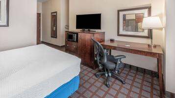 Una habitación de hotel con una cama, un escritorio con televisor, una silla, un microondas y una lámpara.