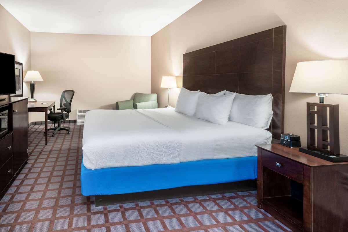 A hotel room with a large bed, a desk with a chair, a television, and two lamps.