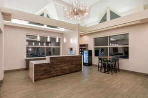 Ein moderner Empfangsbereich mit einem Holzbüro, einer Sitzecke mit Stühlen, einem Kühlschrank und Pendelleuchten.