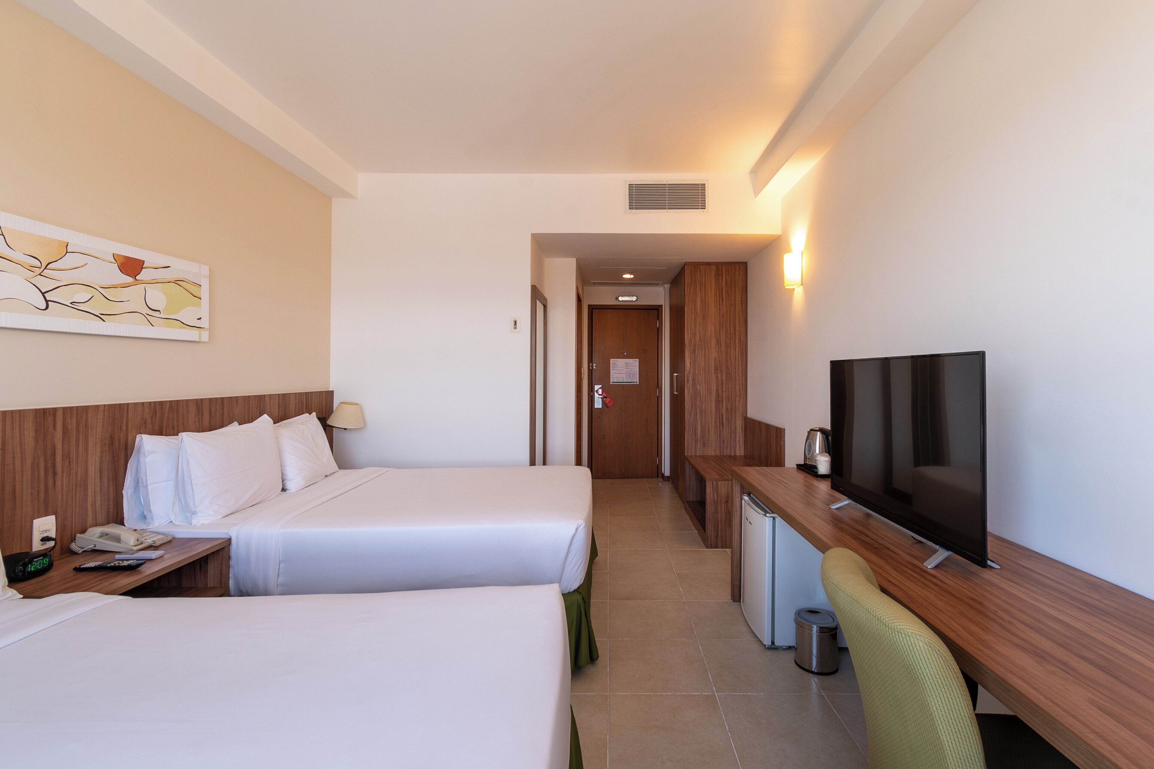 Una habitación de hotel con dos camas, un escritorio con televisor y una kitchenette pequeña.