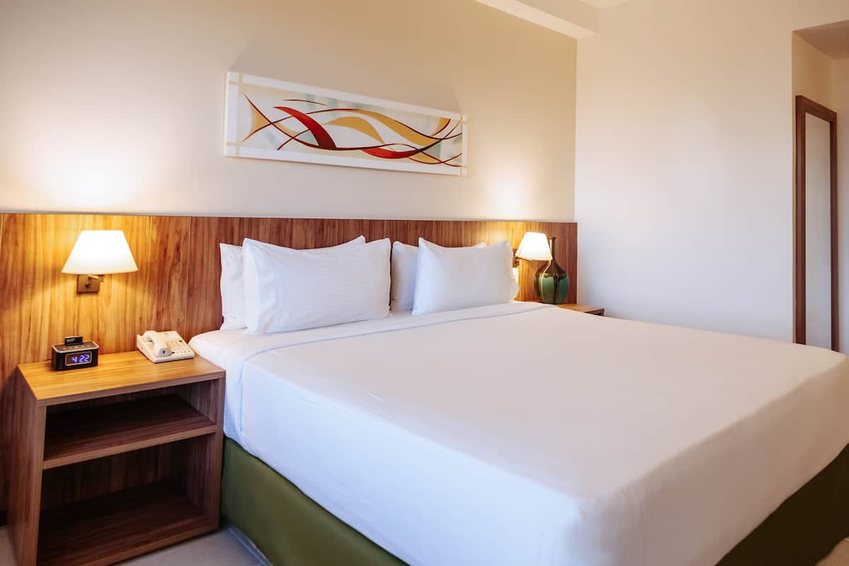 A hotel room with a large bed, wooden headboard, bedside lamps, a telephone, and a wall art piece.