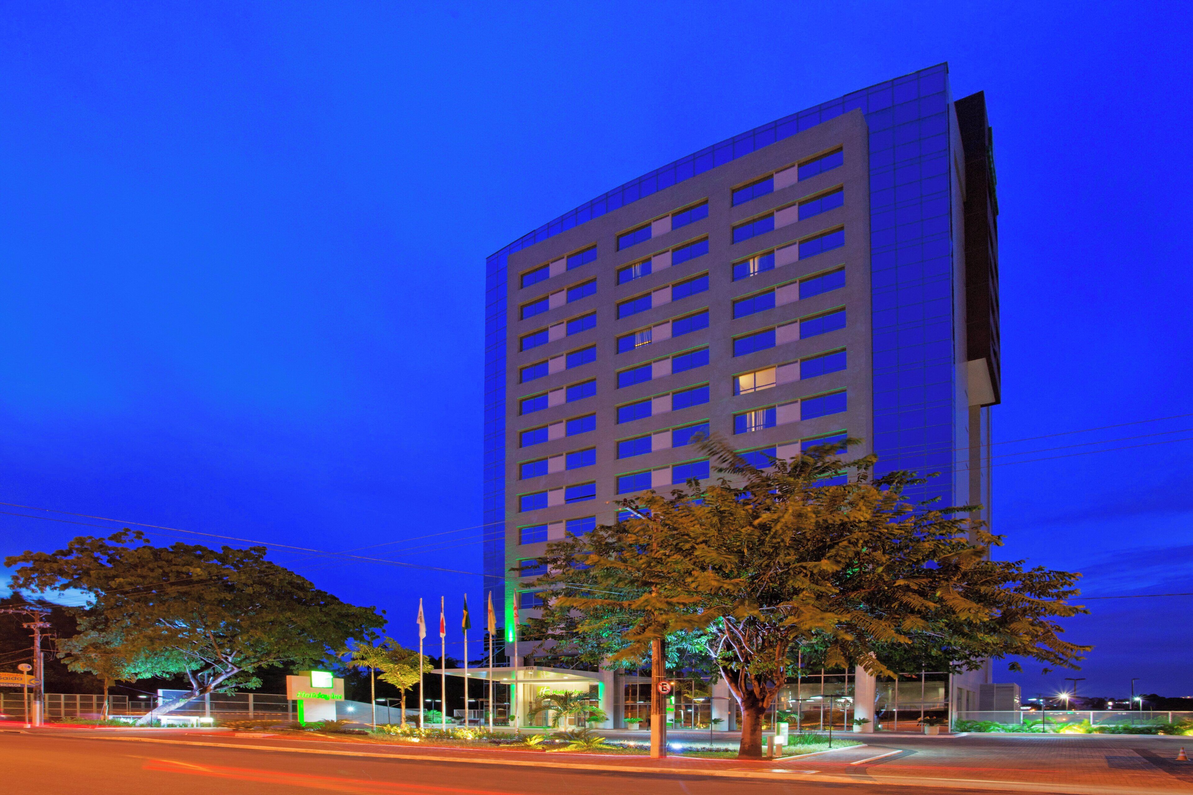 A high-rise building with multiple floors, a well-lit entrance, and a landscaped area with trees.