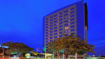 A high-rise building with multiple floors, a well-lit entrance, and a landscaped area with trees.