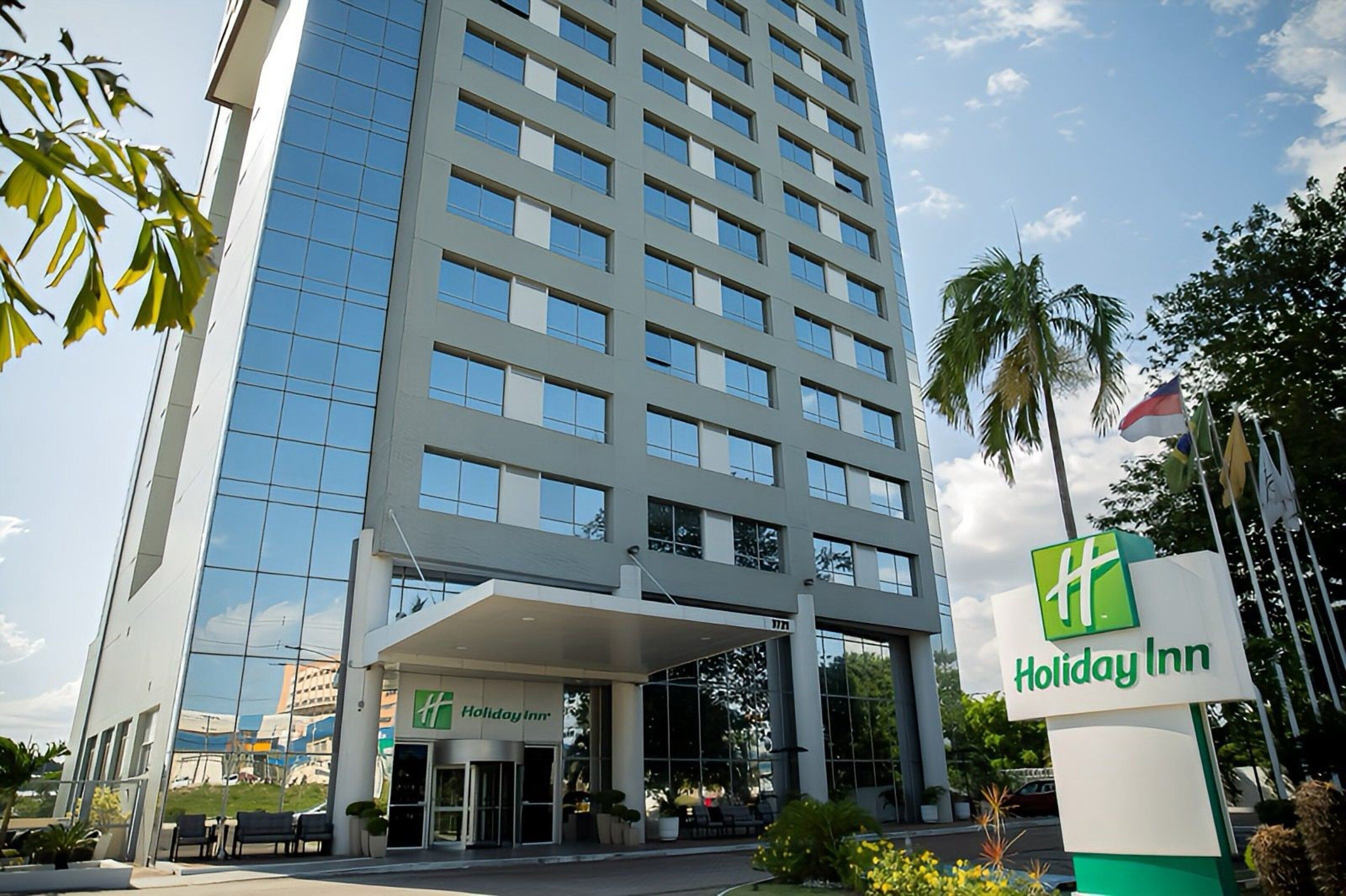 Ein Holiday Inn Hotel mit moderner Glasfassade, überdachter Einfahrt und einem Schriftzug.