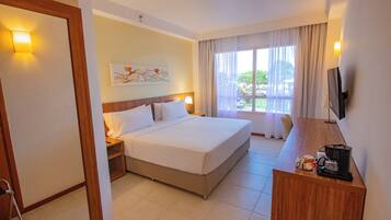 Quarto de hotel com uma cama grande, mesas de cabeceira, escrivaninha com cafeteira, televisão e janela com cortinas.