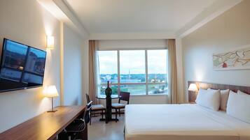 Une chambre d’hôtel équipée d’un lit, d’un bureau, de chaises, d’une télévision et d’une grande fenêtre donnant sur un beau paysage.