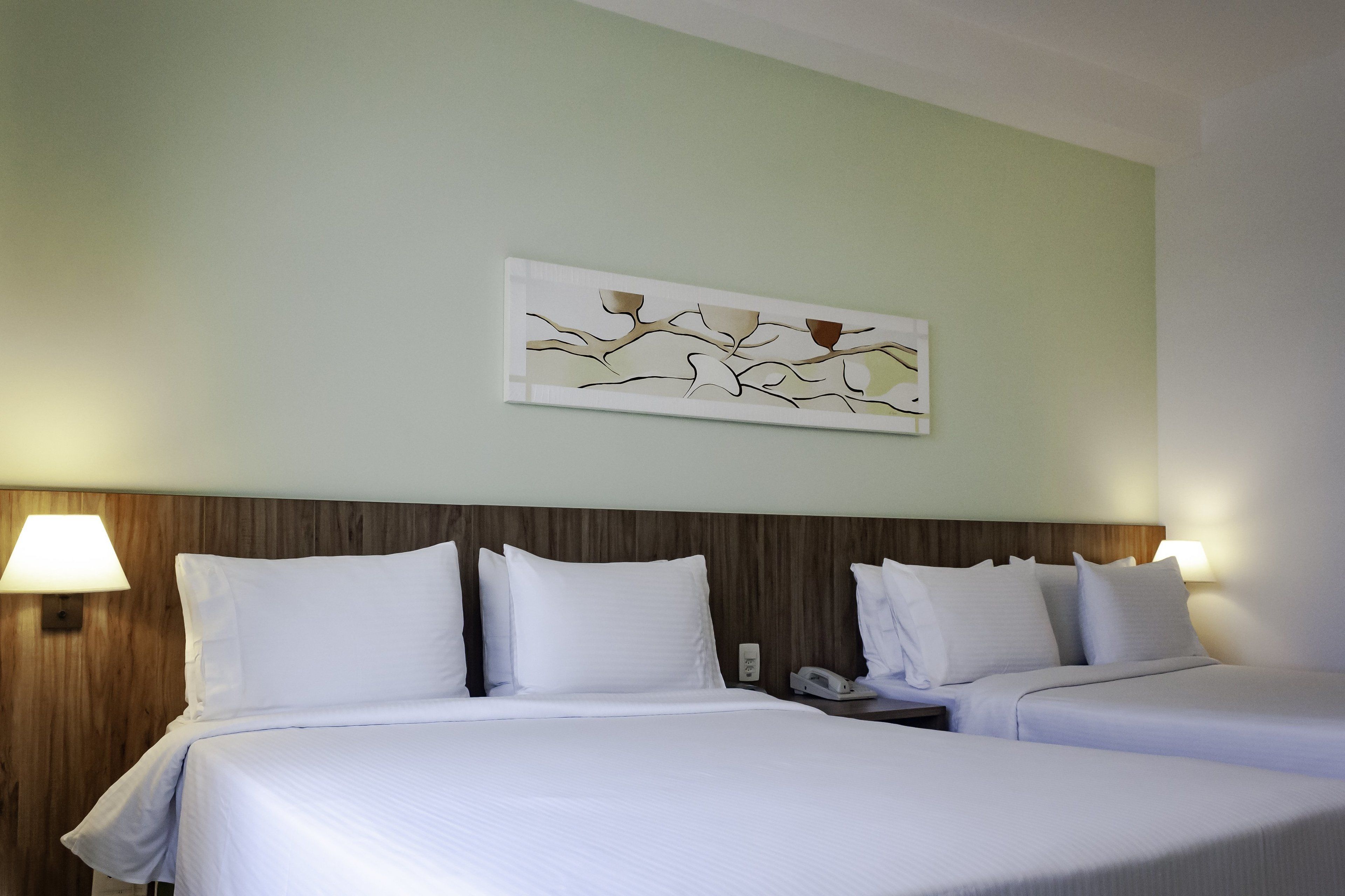 Habitación de hotel con dos camas, cabecero de madera, una obra de arte colgada en la pared y lámparas de noche.