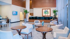 Un hall de hotel con sofás blancos, mesas redondas y una recepción.