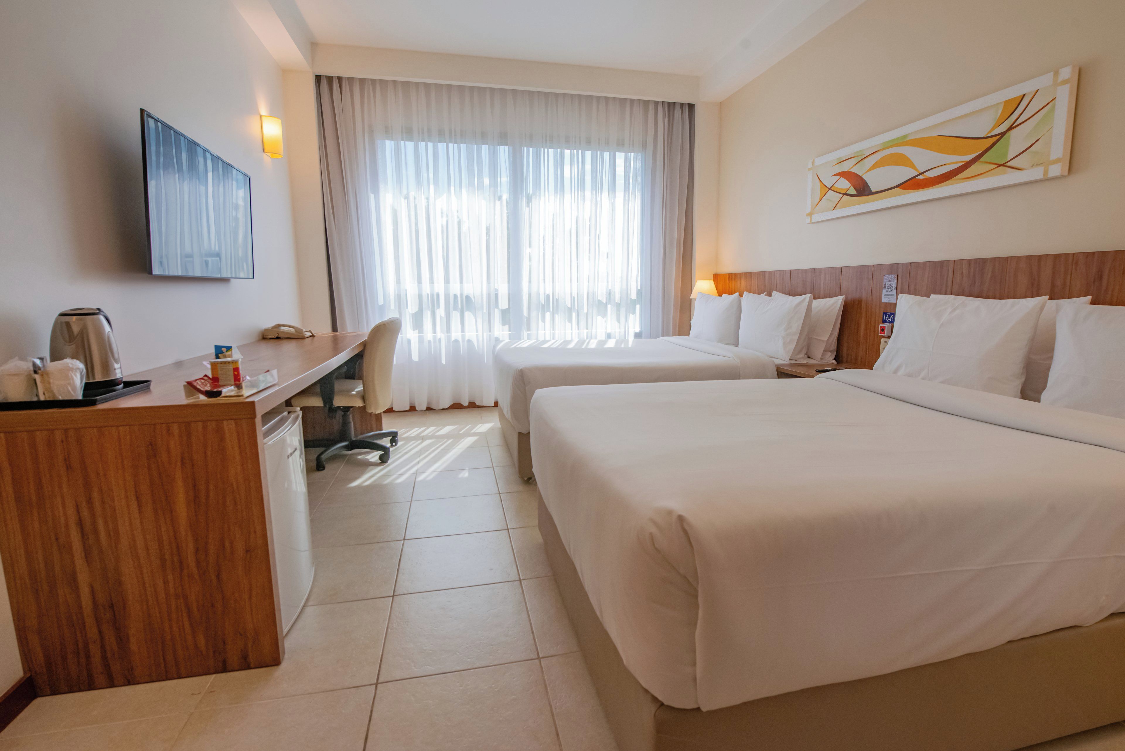 Habitación de hotel con dos camas, un escritorio, un televisor y una ventana con cortinas.
