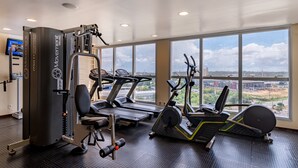 Un gimnasio con cintas de correr, elíptica y máquinas de pesas, amplias ventanas con vista a la ciudad.