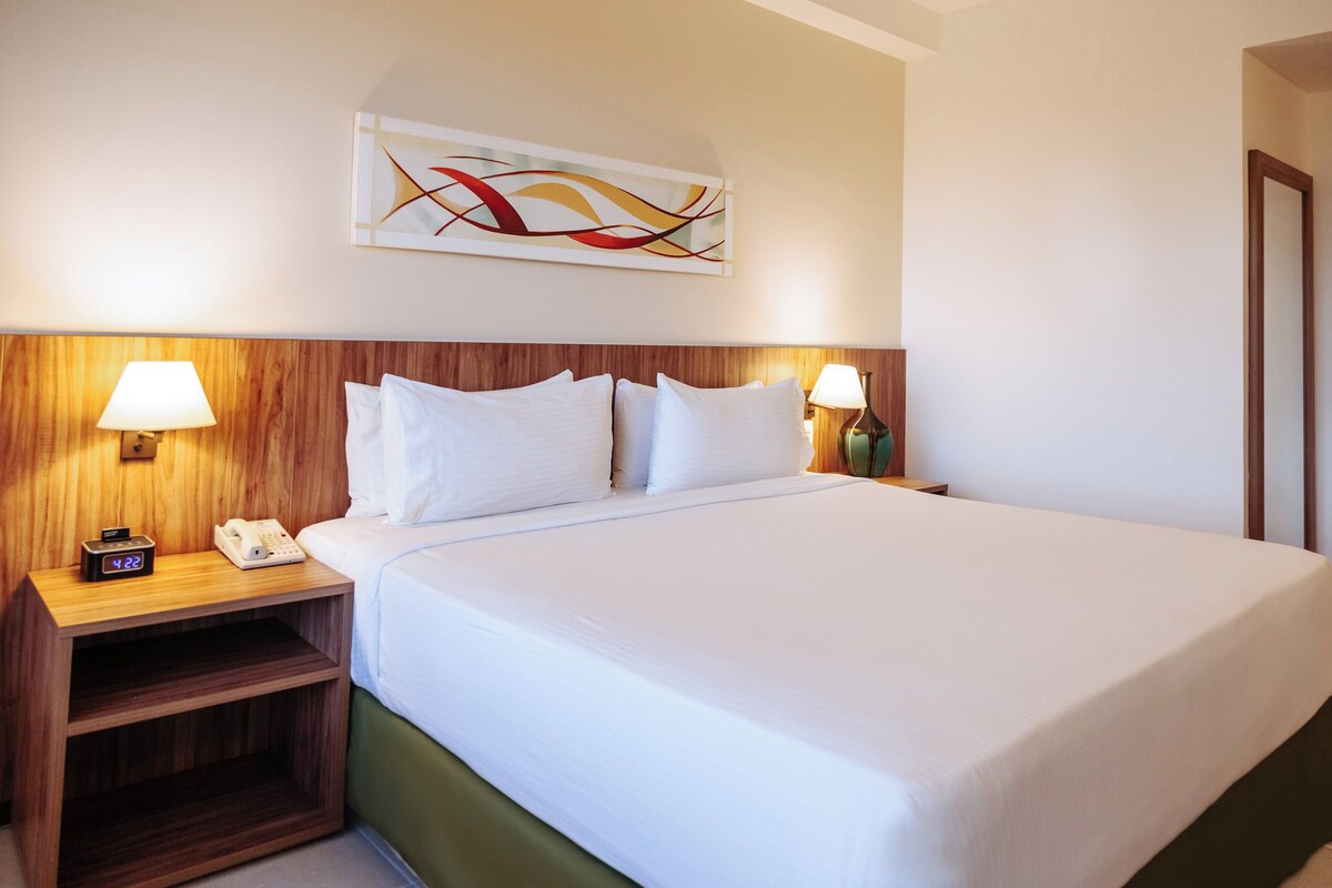 Une chambre d’hôtel avec un grand lit, une tête de lit en bois, des lampes de chevet, un téléphone et une œuvre d’art murale.