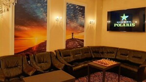 A cozy lounge area with leather sofas, a chess table, and a large TV screen displaying the Hotel Polaris logo. - Hotel Polaris (Swinoujscie)