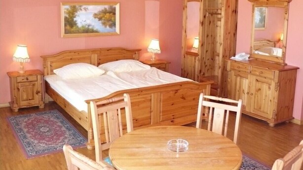 A bedroom with a wooden bed, bedside tables with lamps, a dresser, a round table with chairs, and a painting on the wall. - Hotel Polaris (Swinoujscie)