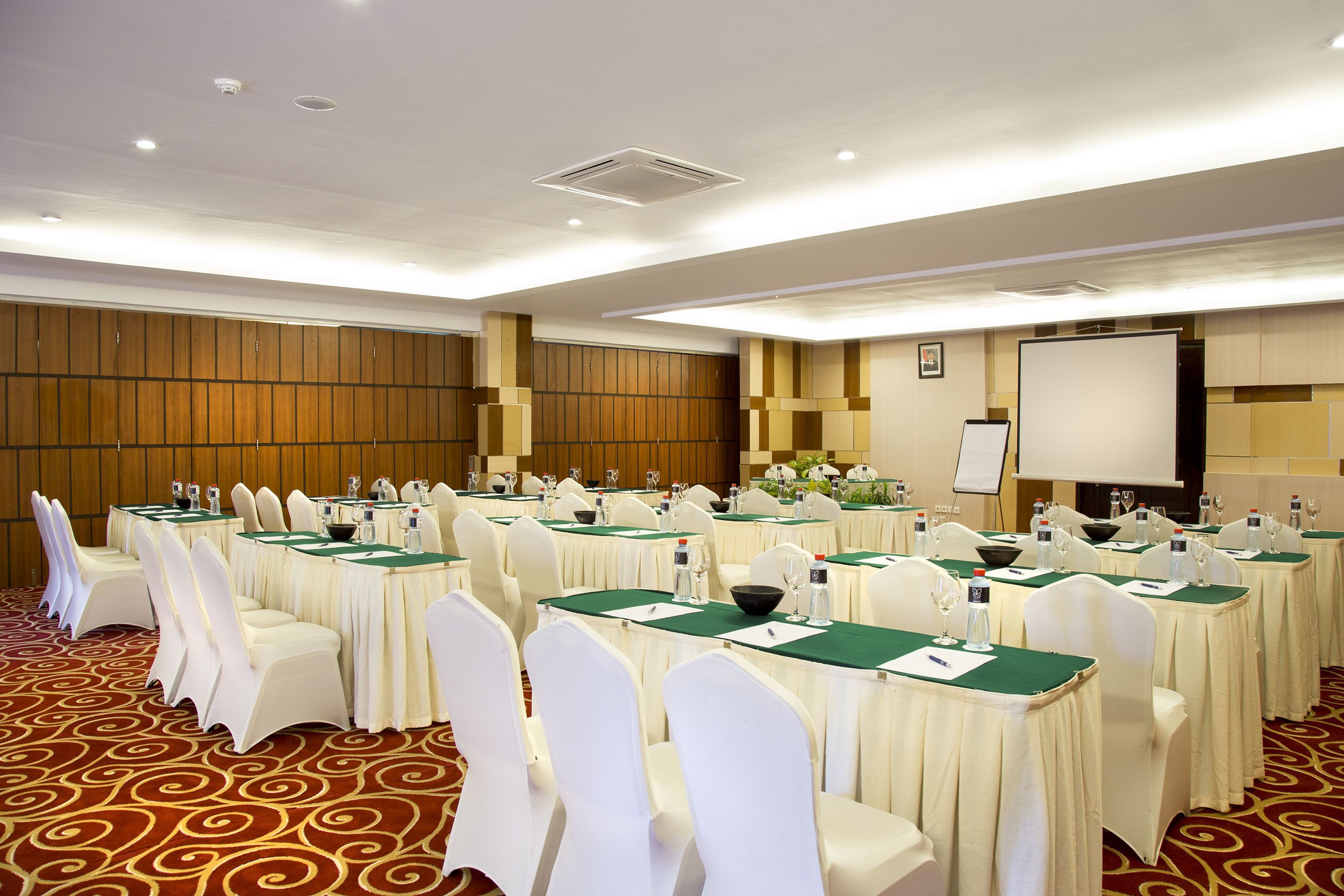 A conference room with multiple tables, white chairs, and a projector screen.