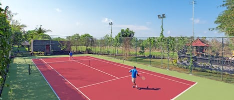 An outdoor tennis court with two players, surrounded by a fence and greenery.