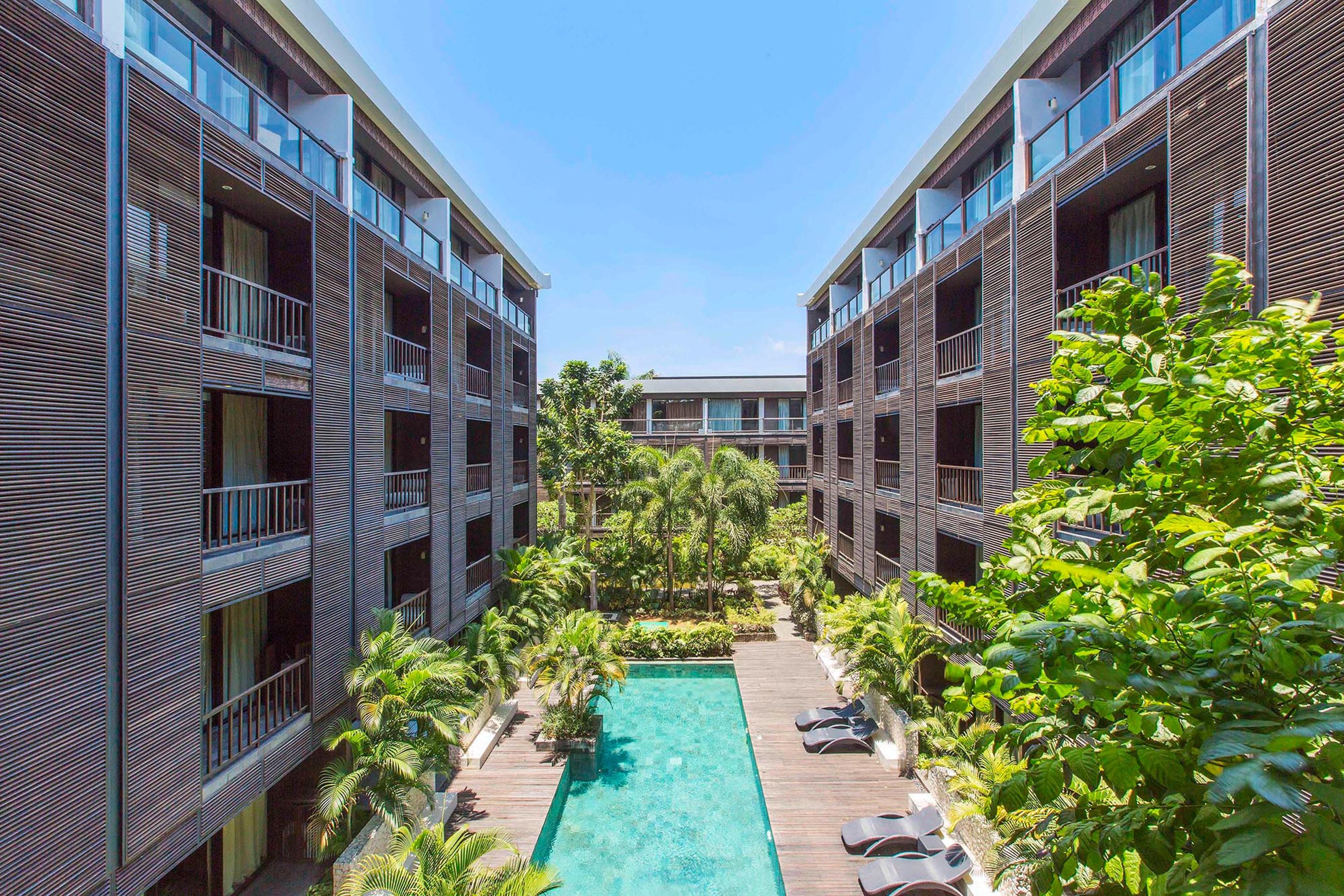 Un hotel moderno con piscina central rodeada de abundante vegetación y múltiples balcones.