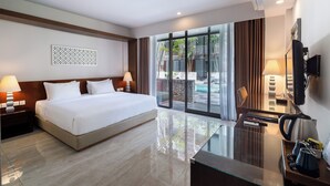 A modern hotel room with a large bed, a glass coffee table, a TV, and a view of the outdoor pool area.