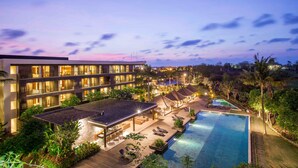 A hotel with multiple floors, outdoor pool, lounge areas, and a well-lit garden.