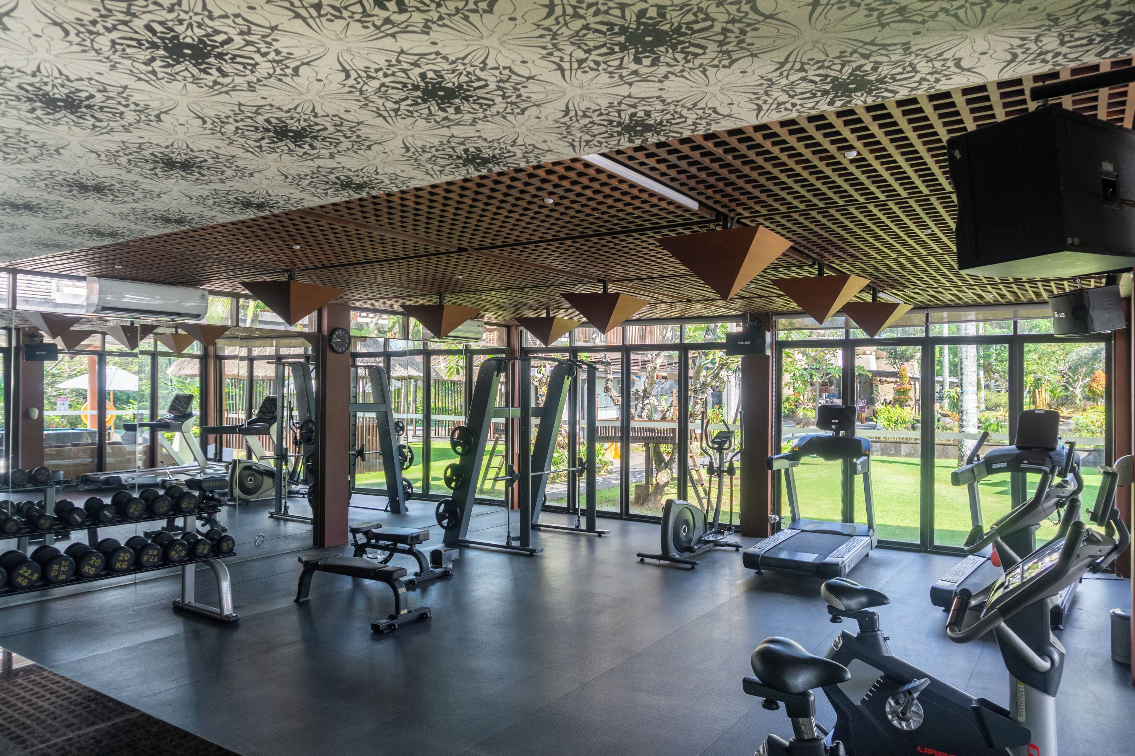 A gym with exercise equipment, large windows, and a patterned ceiling.