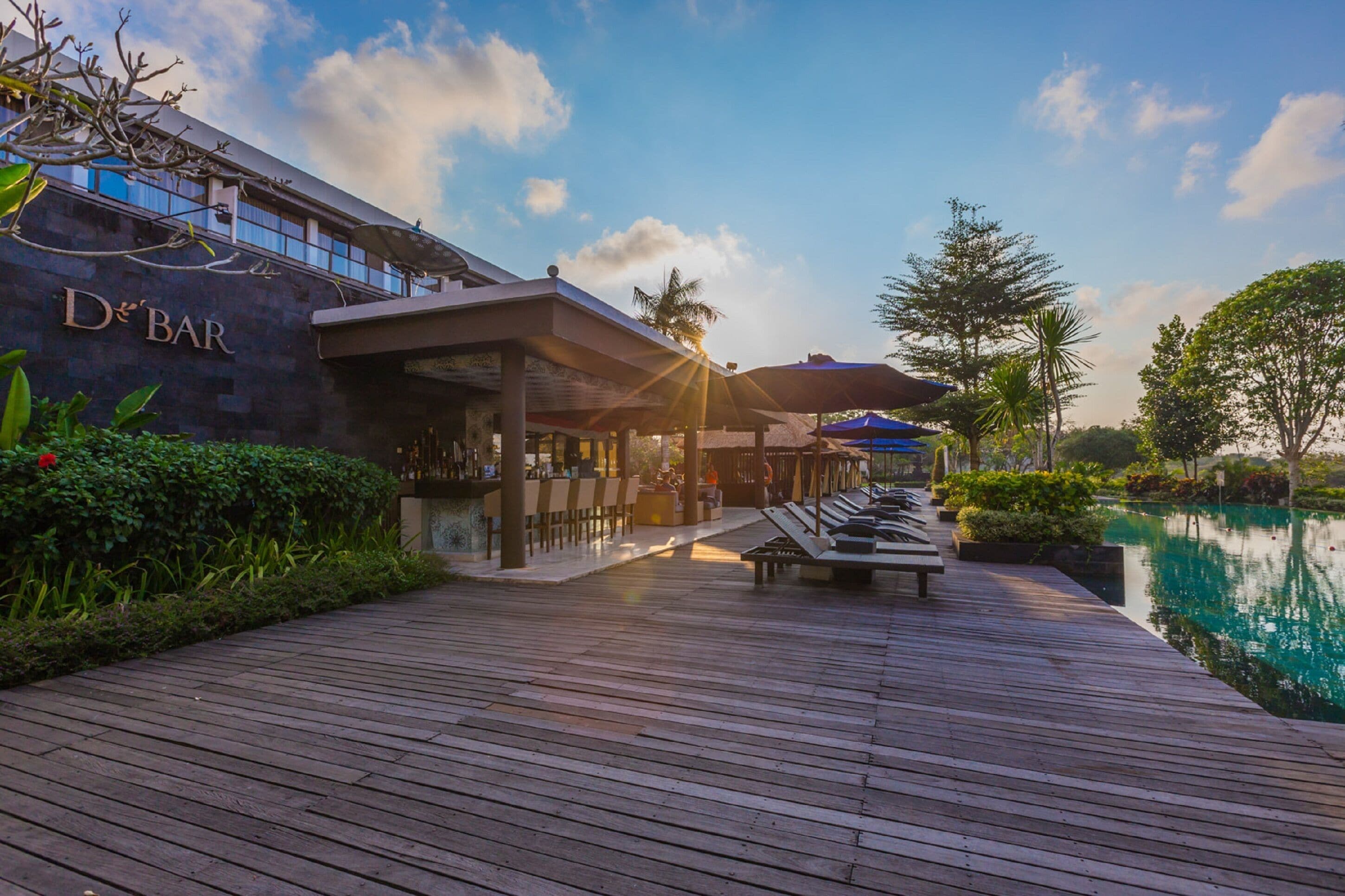 Eine Holzterrasse mit Liegestühlen und einer Poolbar namens 'De Bar'.