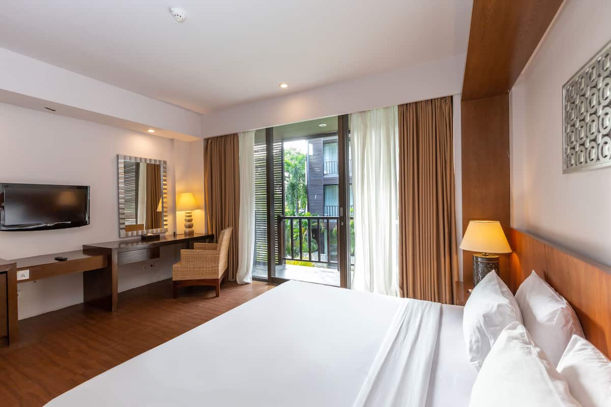 A hotel room with a large bed, a desk, a chair, a TV, and a balcony with curtains.