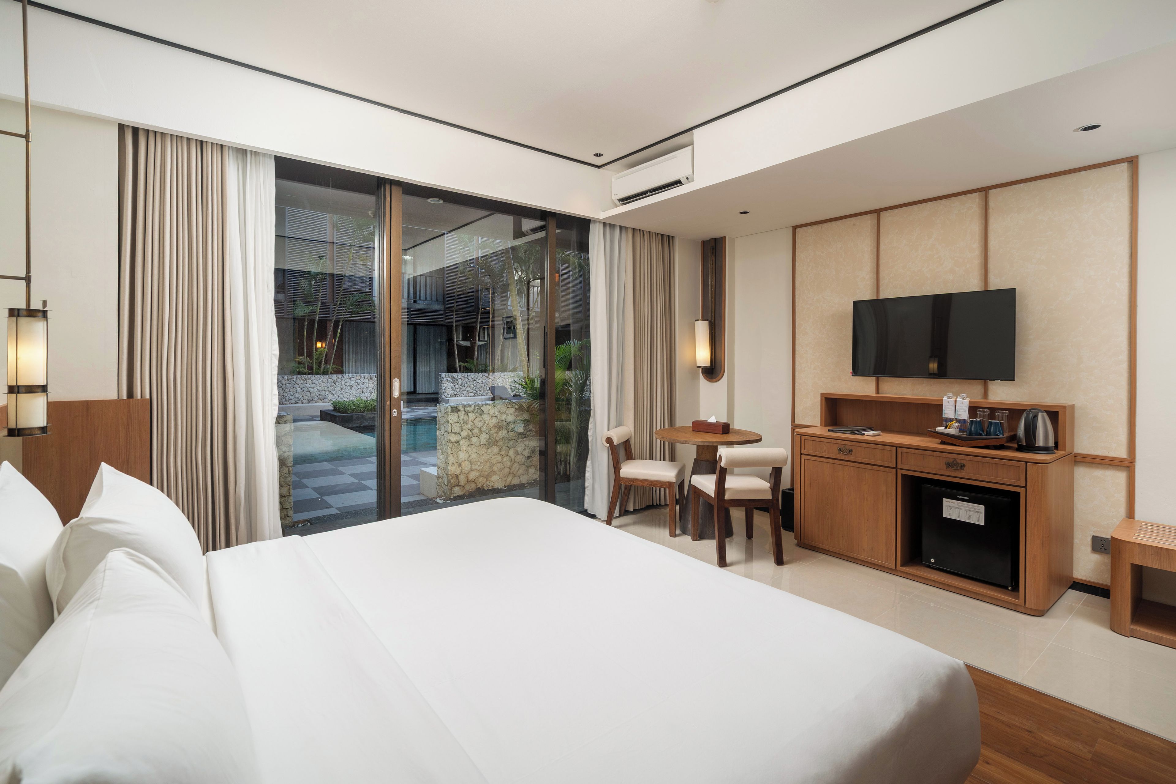 Une chambre d’hôtel avec un grand lit, un bureau avec une télévision, une petite table et une vue sur une piscine et un espace extérieur.
