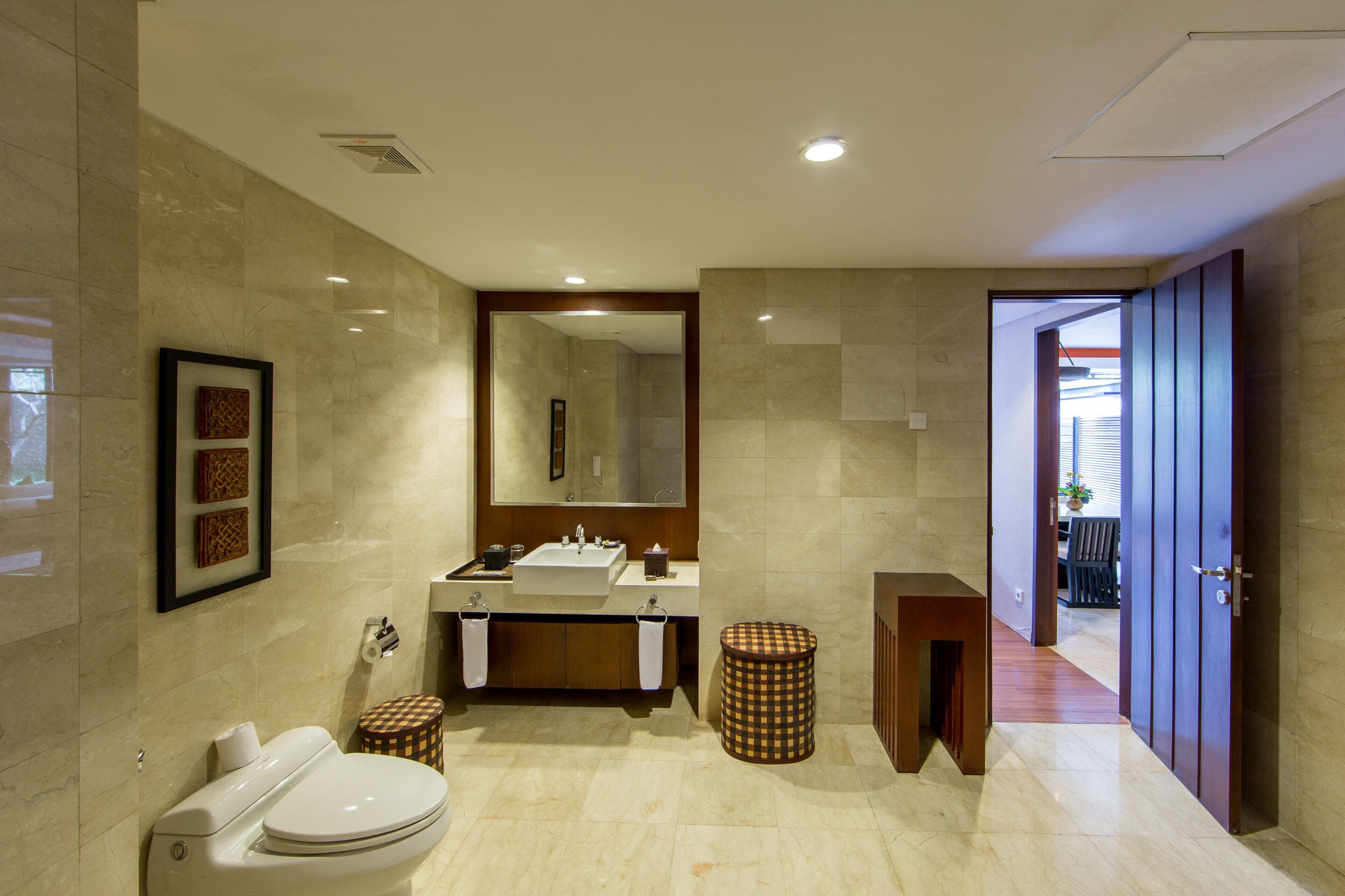 Une salle de bain moderne avec des toilettes, un lavabo et un miroir. On y trouve deux tabourets et une petite table.