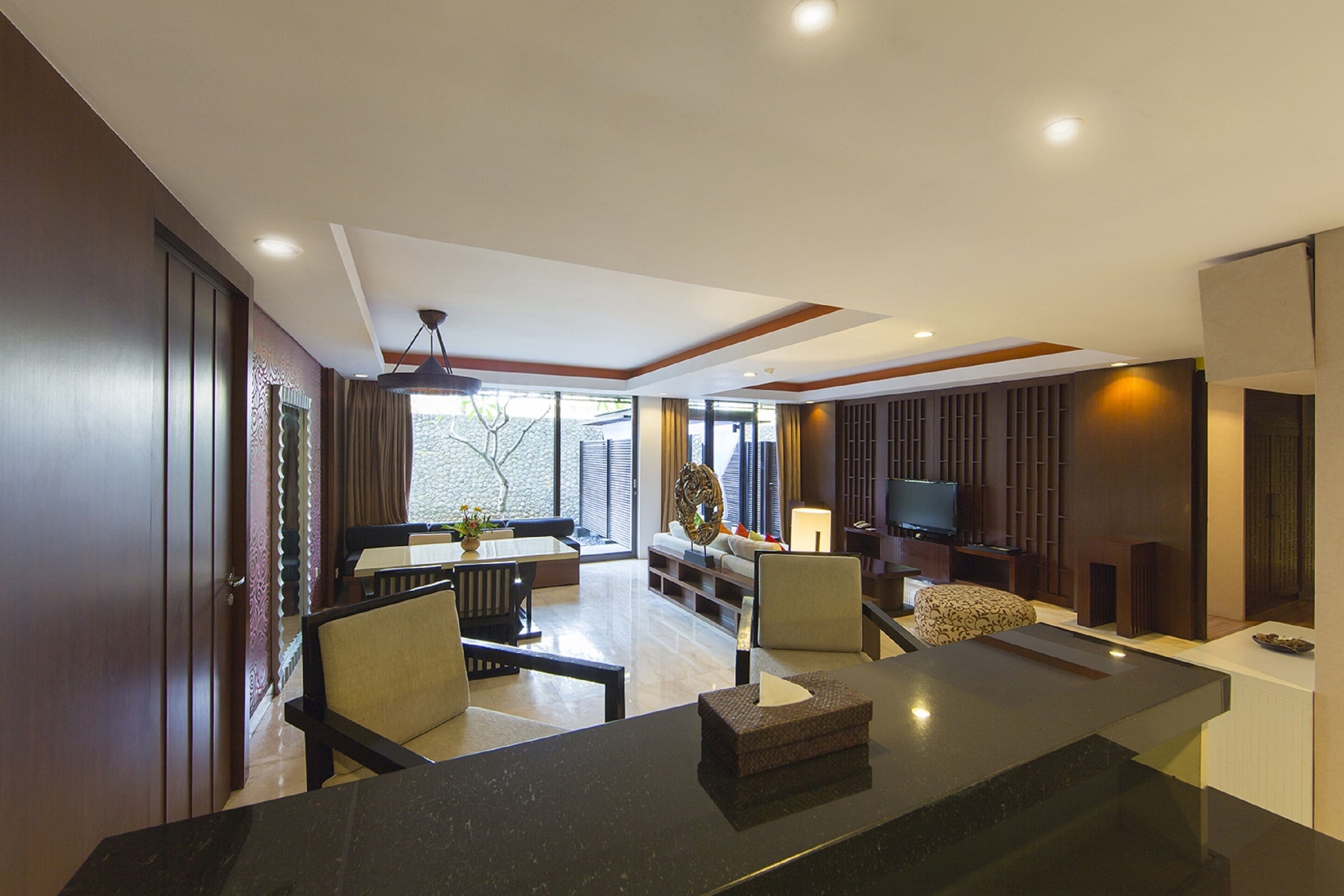 A modern living room with a dining area, a flat-screen TV, and a large window providing natural light.