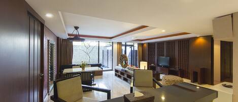 A modern living room with a dining area, a flat-screen TV, and a large window providing natural light.