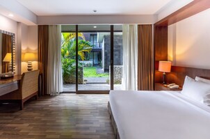 A hotel room with a bed, bedside table, lamp, and a view of a garden through a glass door.
