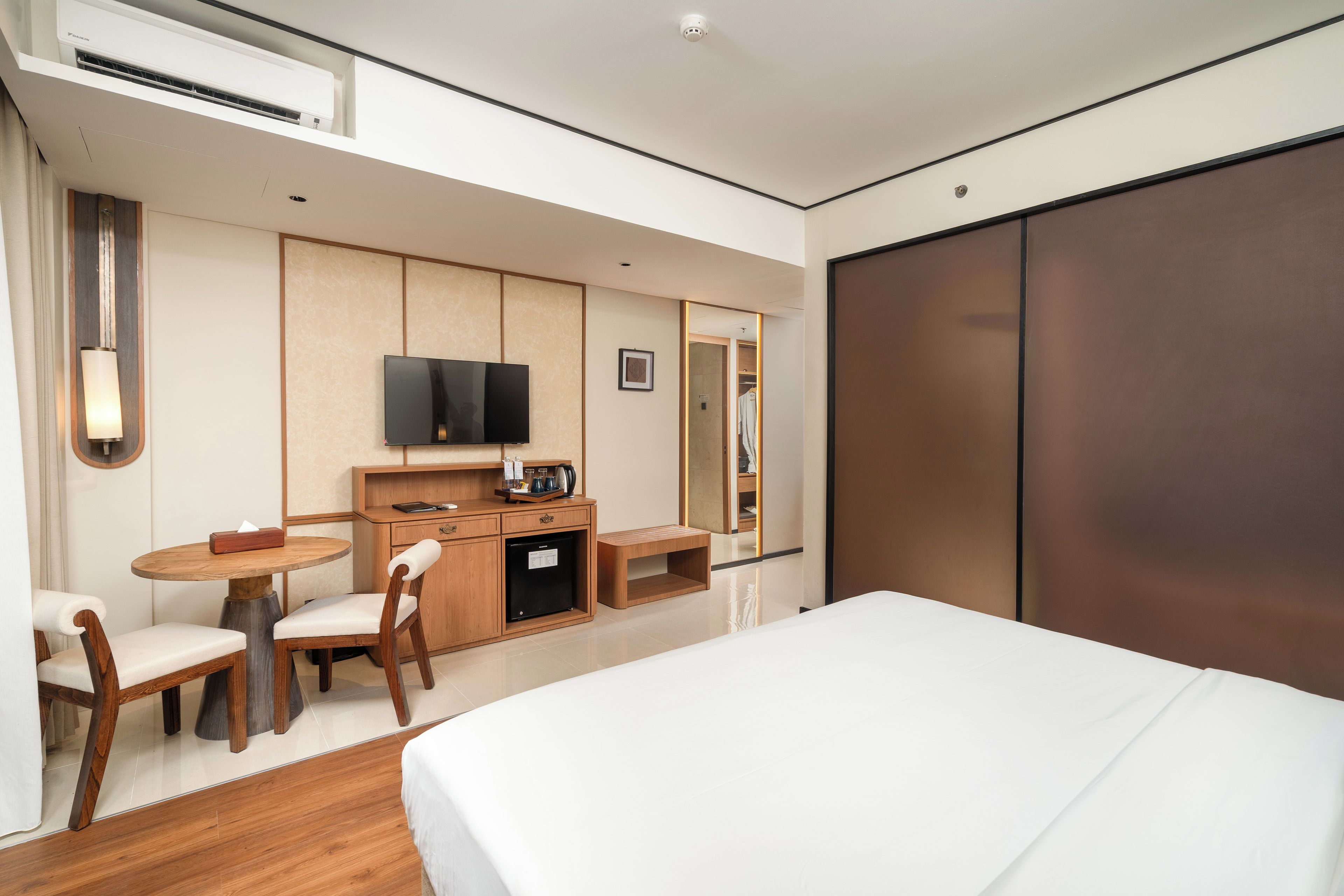 A hotel room with a bed, a desk with a chair, a television, and a wardrobe.