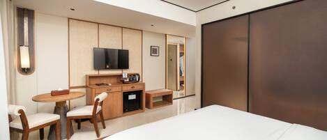 A hotel room with a bed, a desk with a chair, a television, and a wardrobe.