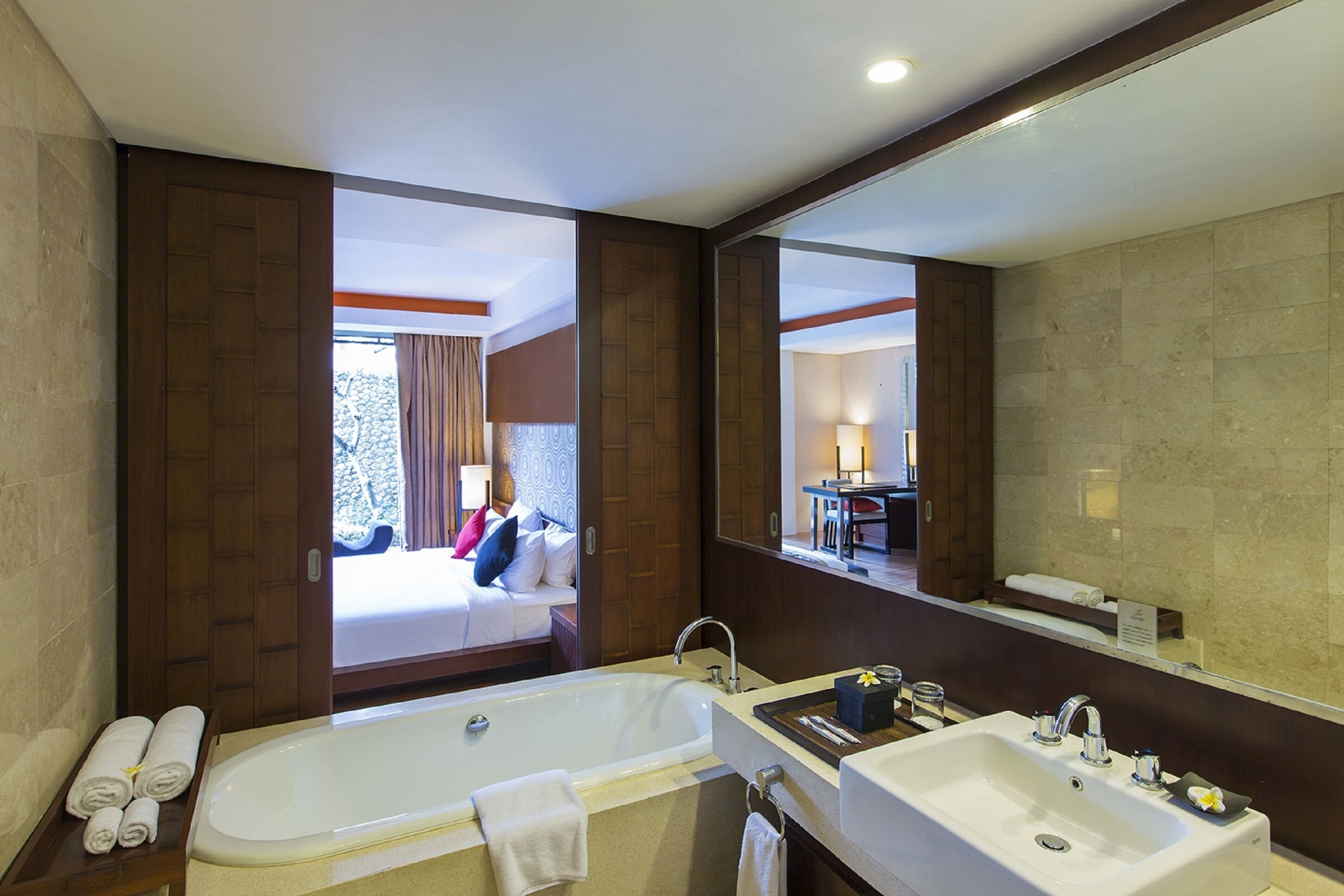 A modern hotel bathroom with a large bathtub, two sinks, and a mirror reflecting the room.