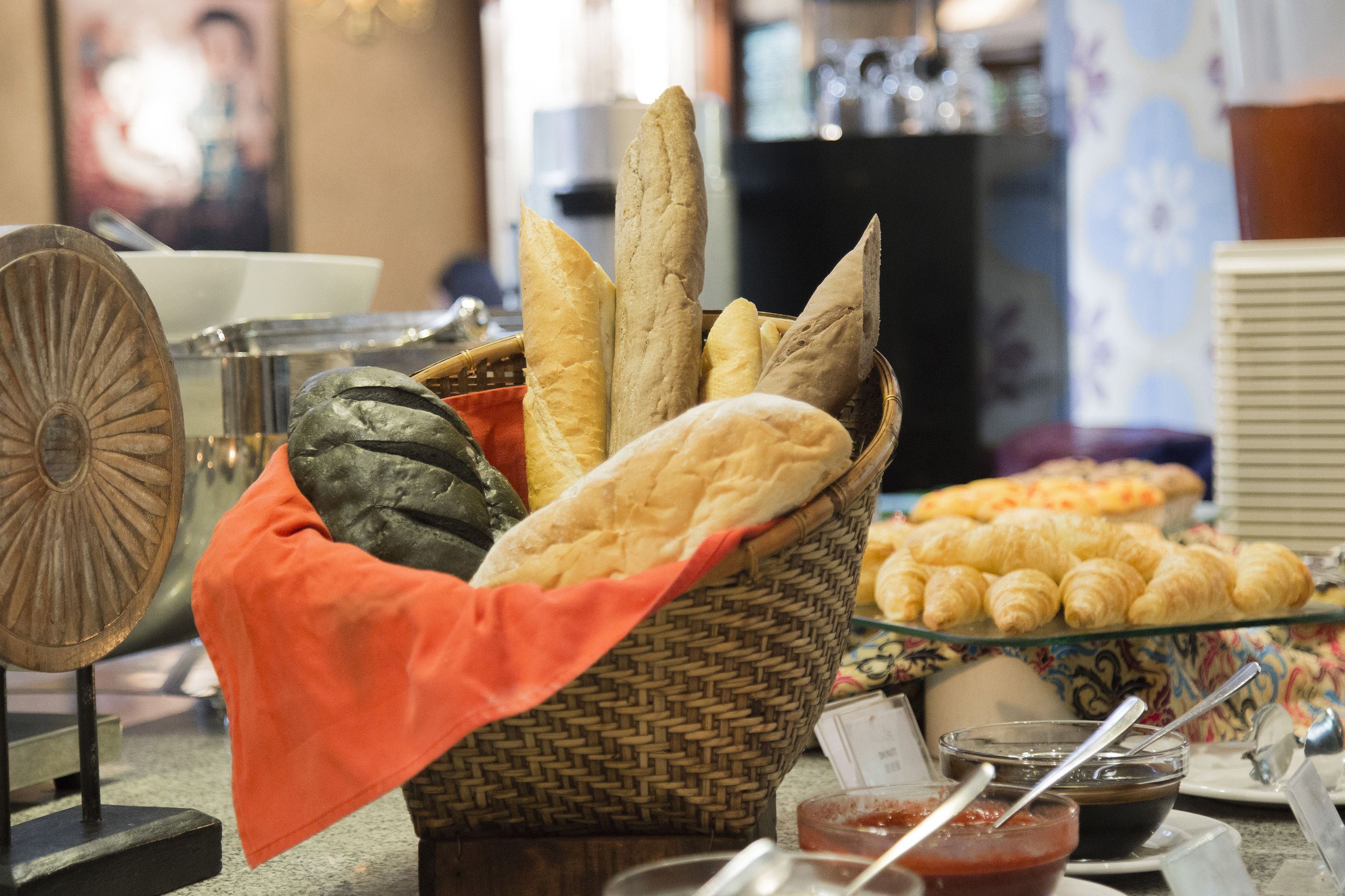 A basket of various breads and pastries, a bowl of jam, and a glass display case with more pastries.