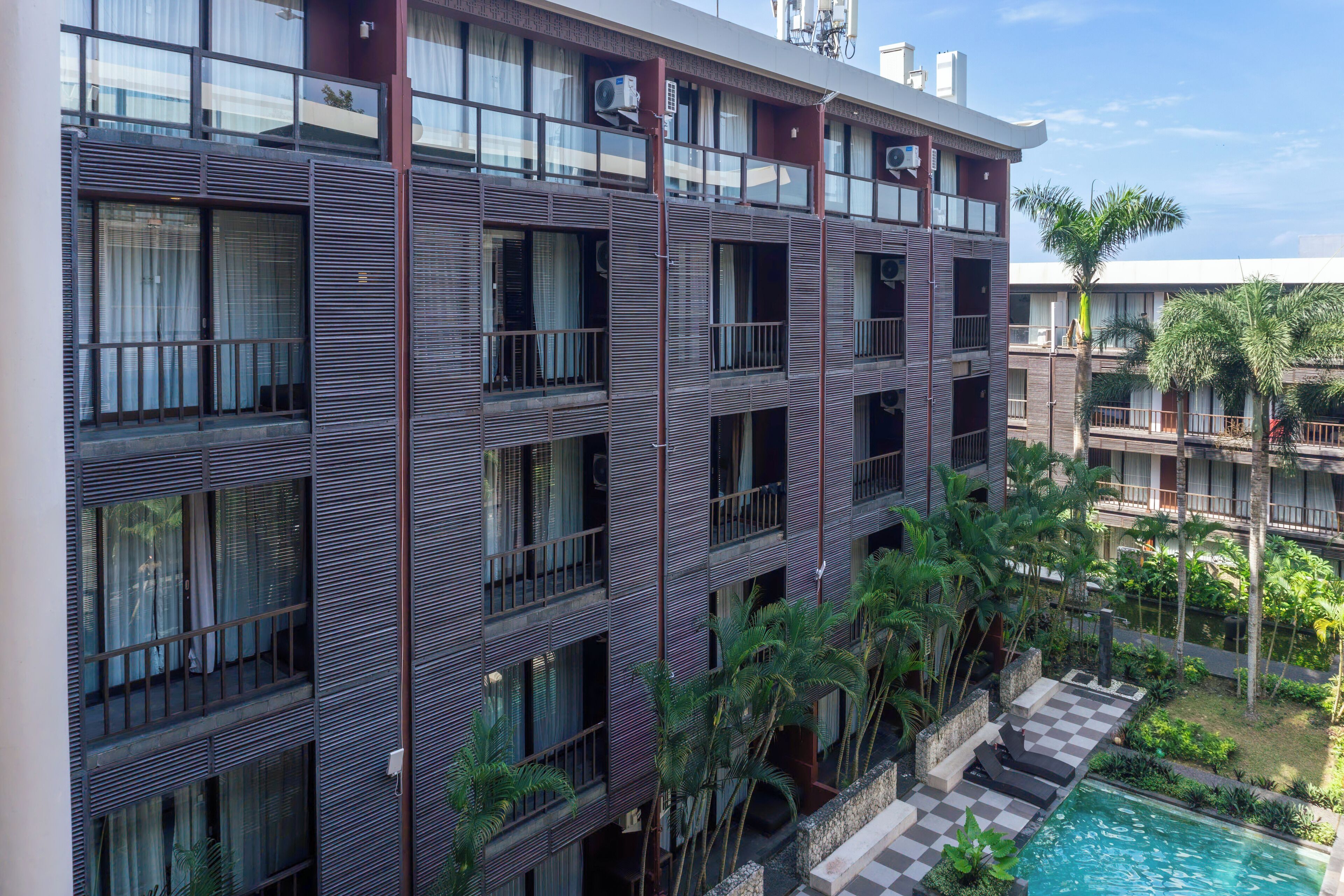 A multi-story hotel with balconies, air conditioning units, and a pool area with palm trees.