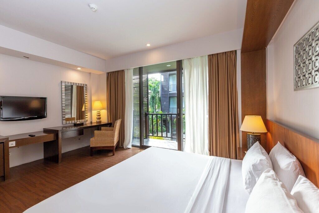 Habitación de hotel con una cama grande, un escritorio con silla, televisor y balcón con cortinas.