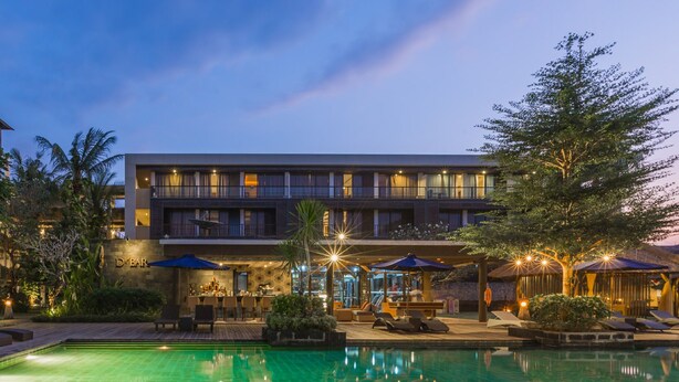 A hotel with a pool, outdoor seating, and a well-lit facade.